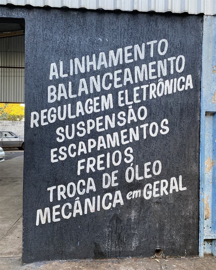 Parede da oficina Udi Mais com a lista de serviços: alinhamento, balanceamento, regulagem eletrônica, suspensão, escapamentos, freios, troca de óleo e mecânica em geral